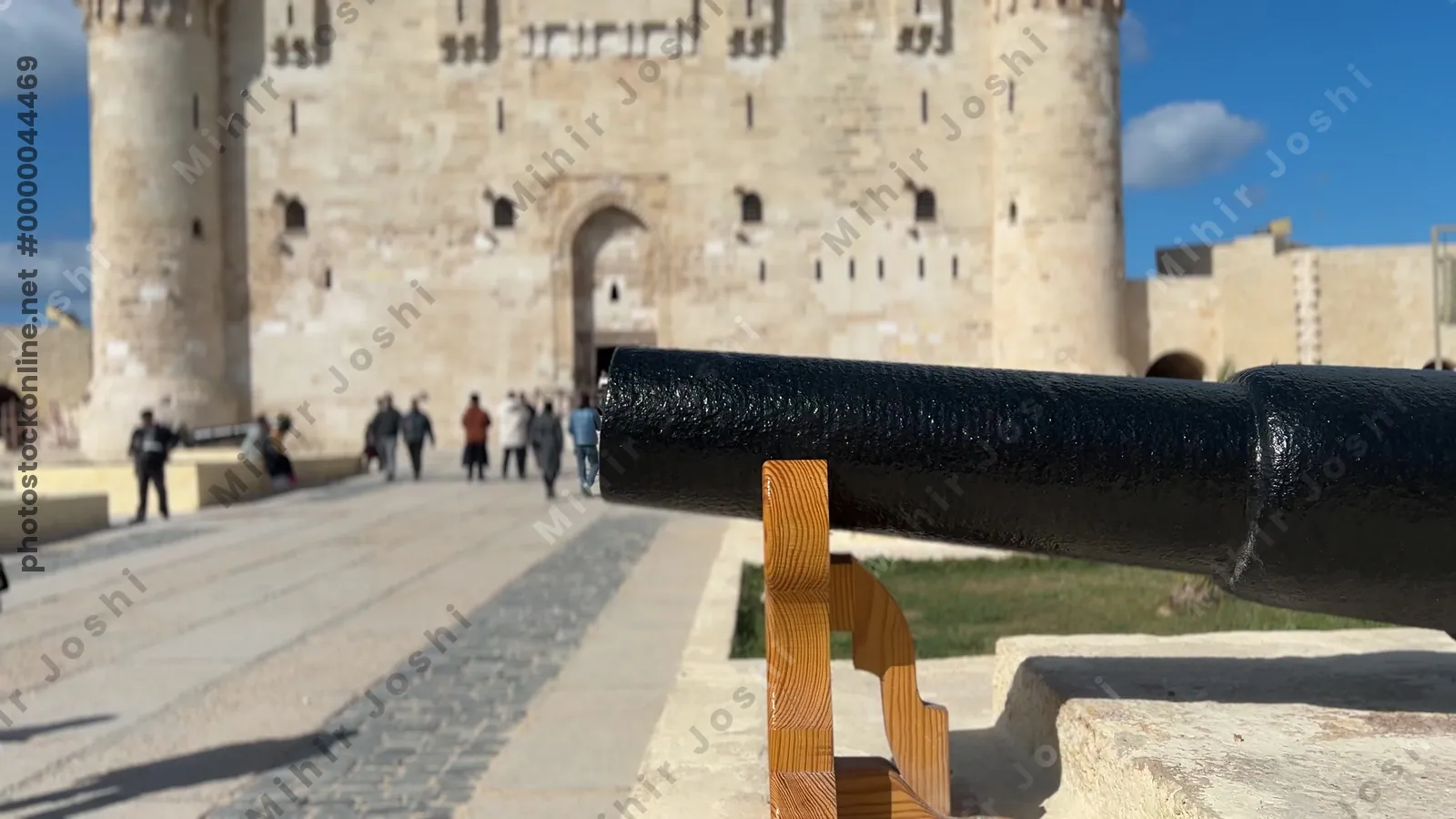 Alexandria, Egypt - Feb 13, 2025: Visitors walk near the main entrance of the Citadel of Qaitbay fortress with cannons displayed at the historic medieval stronghold.