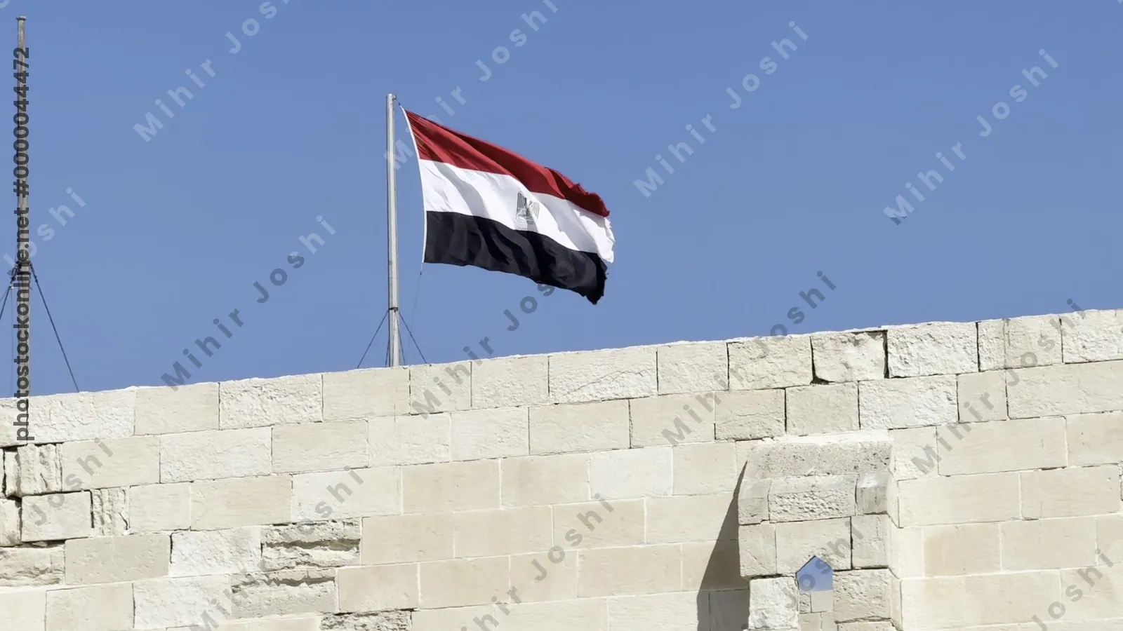 Alexandria, Egypt - Feb 13, 2025: Egypts national flag flying above the fortified wall of the Citadel of Qaitbay, a medieval stronghold on the Mediterranean coast.