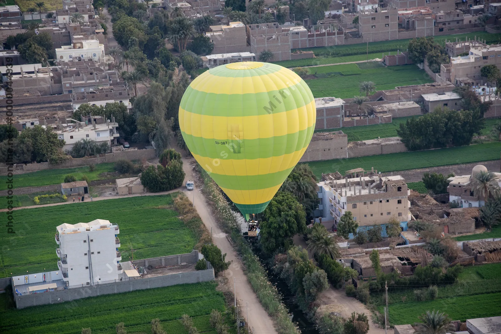 Hot air balloon hovers above lush farmland and traditional houses near Luxor, Egypt, during sunrise